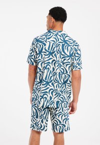 Conjunto de camisa de manga corta y pantalones cortos en crema con patrones en espiral azules. Hecho de tejido ligero con un corte relajado.