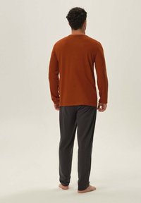 Brązowa bluzka z długim rękawem i ciemnoszare spodnie, obie wykonane z miękkiego materiału. Strój ma luźny krój i minimalistyczny design.