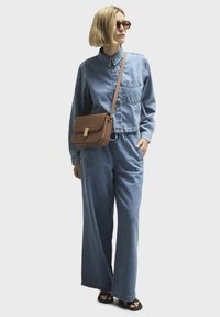 Denim jacket and wide-leg pants in light blue denim. Brown crossbody bag with a clasp detail. Black sandals. Brown sunglasses.