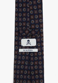 Corbata azul marino con patrones geométricos de paisley en marrón y beige, con una etiqueta blanca cosida que presenta una calavera y huesos cruzados junto con el nombre de la marca "Scalpers".