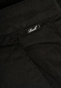 Pantalones de mezclilla negra con una textura suave, que presentan una etiqueta de marca visible y costuras en contraste a lo largo de las costuras.