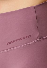 Højtaljede leggings i mauve, med en glat tekstur og flade sømme. "SWEDEMOUNT" logoet i en mørkere nuance trykt på taljen.