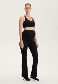 Zwarte sporttop en uitlopende legging, gemaakt van rekbare stof. De outfit is ontworpen voor comfort, met een soepele textuur en een getailleerde pasvorm.