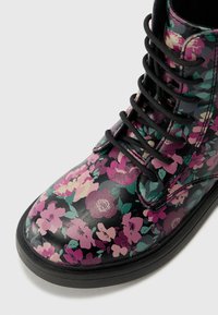 Bota de tobillo floral con base de cuero negro, con flores multicolores en rosa, púrpura y verde. Cierre de cordones negros y suela de goma.