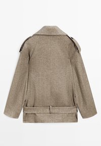 Beige linnedjakke med skulderstropper, bred krave, lange ærmer og bælte i taljen, vist bagfra på hvid baggrund.