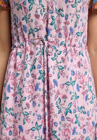 Rochie florală realizată dintr-un material roz deschis, cu un model vibrant de flori albastre și roz, talie strânsă cu un detaliu de șnur.
