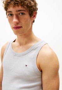 Jasnoszary bawełniany top bez ramiączek z prążkowaną teksturą, charakteryzujący się okrągłym dekoltem i małym znakiem na lewej stronie klatki piersiowej.