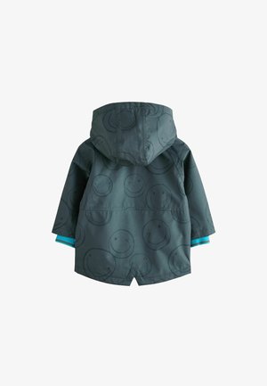 Sötétzöld kapucnis dzseki, mosolygó arc mintázattal, türkiz ujjakkal és vízálló textúrával.