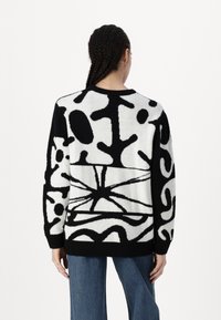 Pull noir et blanc avec des motifs abstraits, fabriqué en tissu doux et texturé, doté d'un col rond et de manches longues.