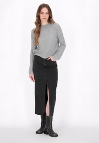 Grijze gebreide trui en zwarte denim rok met een voorkapsel, gecombineerd met zwarte enkellaarzen. Eenvoudig ontwerp, gestructureerde stof en casual pasvorm.