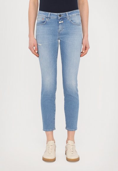 Lyseblå, slim-fit jeans med mellemhøj talje, der har diskret slidagemønster og whiskering, parret med cremede sneakers.