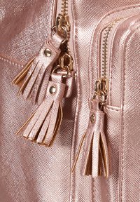 Dettaglio di una borsa in rosa dorato metallico con due zip con accentuazioni a frangia, finitura texture e hardware metallico visibile.