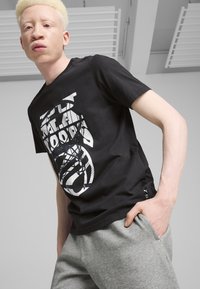 Sort bomulds T-shirt med et stort hvidt grafisk design, rund udskæring og korte ærmer. Matchet med grå sweatpants.