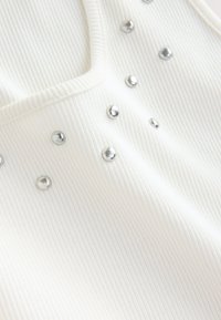 Tissu blanc côtelé orné de clous argentés en accents décoratifs, disposés de manière aléatoire à l'avant, créant texture et intérêt visuel.