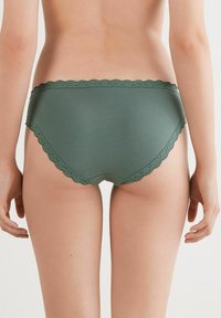 Groene katoenen slips met golvende kantafwerking langs de tailleband en beenopeningen. Soepele textuur, middelhoge pasvorm en minimale bedekking.