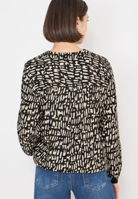 Langærmet top i sort med et beige abstrakt mønster, med rund halsudskæring og opsamlede manchetter, lavet af et glat stof.