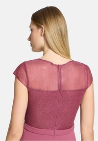 Robe cintrée avec un haut transparent et scintillant magenta, une ceinture unie, des manches courtes et une fermeture éclair au dos. Texture lisse.