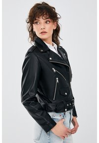 Zwart leren motorjack met zilveren ritsen, drukknoopsluitingen en een ceintuurlijn. Heeft een cropped fit en meerdere met rits afgesloten zakken.
