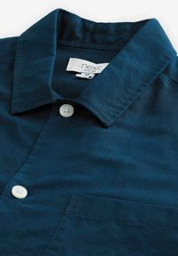 Camicia button-up blu navy con colletto, dotata di taschino sul petto e bottoni bianchi. Realizzata in un tessuto morbido con una leggera lucentezza.