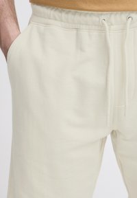 Light beige sweatpants with a drawstring waistband, side pockets, and a soft, textured fabric. Simple, casual design.