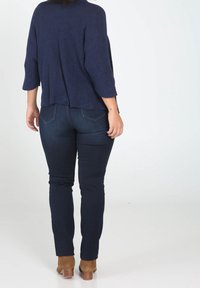 Top de punto navy con mangas de tres cuartos, combinado con jeans de mezclilla oscuros y botas de tacón marrón hasta el tobillo. Presenta un corte holgado y textura de canalé.
