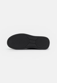 Schwarze Gummisohle mit einem strukturierten Grip-Muster, das eine geschwungene Form und flache Kanten aufweist. Das Design betont Traktion und Haltbarkeit.