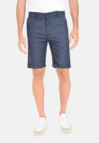 Pantaloni corti blu navy realizzati in un tessuto morbido, con un frontale piatto, chiusura con bottone e orlo arrotolato. Abbinate a sneakers bianche.