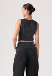 Gilet en denim noir cropped sans manches, associé à un pantalon en denim noir taille haute et ample. La vue arri�ère met en avant les détails de couture.