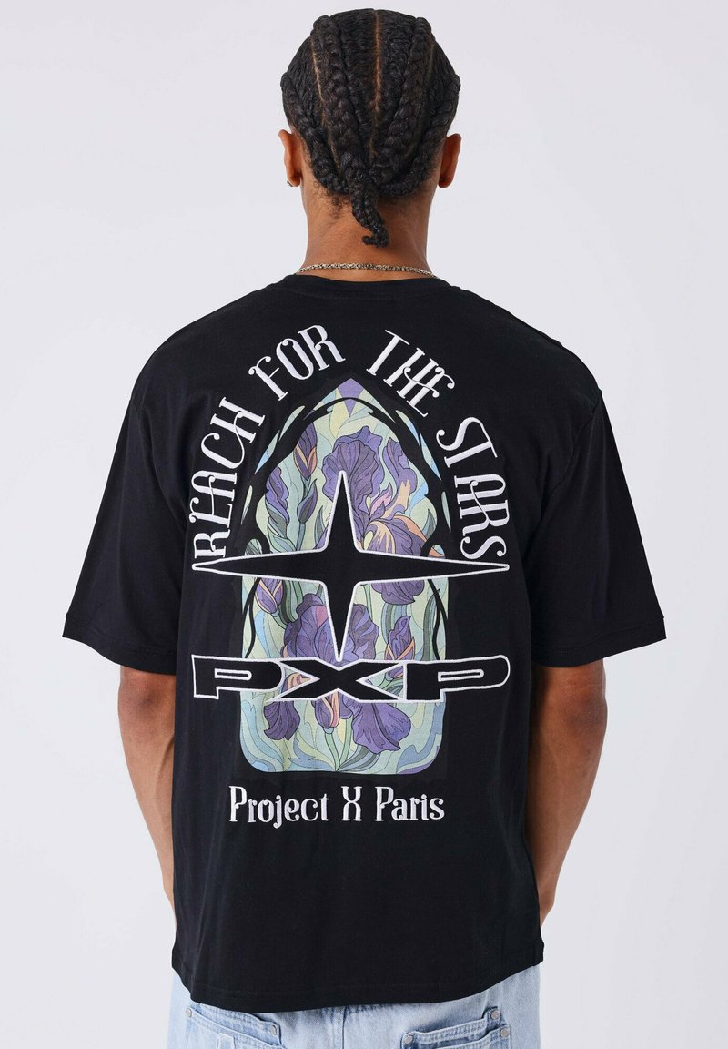Camiseta de algodón negra con un gran gráfico en la parte posterior con diseño floral, el texto "Alcanza las Estrellas" y "Project X Paris."