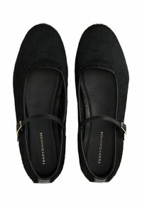 Par de bailarinas negras estilo Mary Jane con una parte superior texturizada, tiras delgadas con hebilla y el logo de Tommy Hilfiger en las plantillas, mostradas desde arriba.