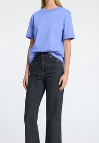 Jasnoniebieska bawełniana koszulka z okrągłym dekoltem i krótkimi rękawami, w połączeniu z ciemnoszarymi dżinsami z wysokim stanem i sznurkiem w pasie.