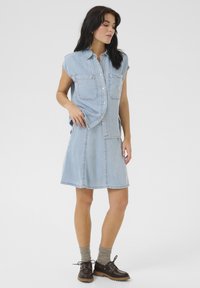Abito in denim azzurro chiaro con un top colletto senza maniche, due tasche sul petto e una gonna a ruota. Presenta cuciture cucite e un orlo dritto.
