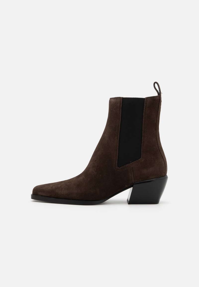 Bottine en daim marron foncé avec panneaux latéraux élastiques noirs, talon bloc incliné et languette à l'arrière sur fond blanc.