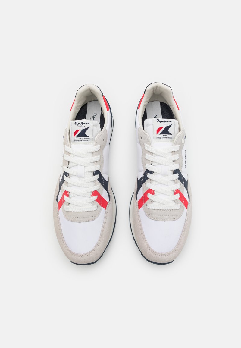 Zapatillas blancas con acentos de ante, rayas rojas y marinas, y una suela texturizada. Los cordones son blancos y el logotipo se muestra en la lengüeta.