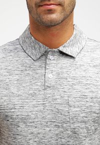 Grijze marl polo shirt met een kraagontwerp, drie knopen en een enkele borstzak. Zachte textuur met een gemêleerd patroon.