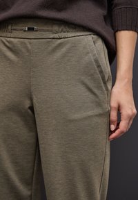 Khaki zúžené kalhoty s texturovanou tkaninou, obsahující boční kapsy a plochý pas, v kombinaci s hnědým pleteným topem.
