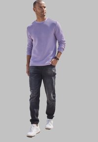 Suéter de punto lila claro, joggers de mezclilla oscura con tobillos ajustados y zapatillas blancas, mostrando un atuendo casual y moderno.