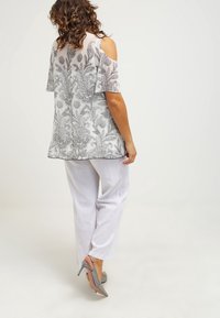 Kevyt, harmaa kukkakuvioinen pitsipaita kylmissä olkapäissä, yhdistetty valkoisiin housuihin ja hopeisiin korkokenkiin. Sujuva pinta, virtaava muotoilu.