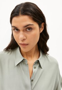 Lichtgroen, collo-shirt met een gladde textuur, knoopsluiting en een losse pasvorm. De stof lijkt zacht en lichtgewicht.