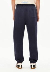 Marineblauwe joggingbroek met een losse pasvorm, elastische manchetten en een enkele achterzak. Gemaakt van zacht materiaal, met een gladde textuur en een minimalistisch ontwerp.