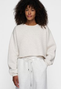 Gepunkteter, hellbeiger, kurz geschnittener Sweatshirt aus weichem, strukturiertem Stoff mit Rundhalsausschnitt und überschnittenen Schultern, kombiniert mit passenden Jogginghosen.