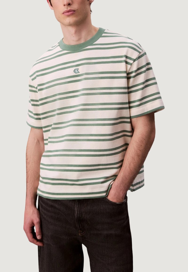 Camiseta de rayas en blanco y verde con cuello redondo, mangas cortas y un logo en el pecho. Confeccionada en tejido suave y con un corte relajado.