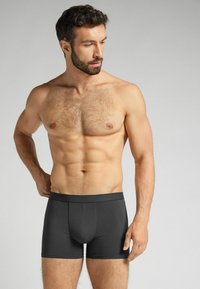 Schwarze Boxershorts aus glattem Material mit engem Sitz, ausgestattet mit einem breiten Bund und einer konturierten Tasche für zusätzlichen Halt.