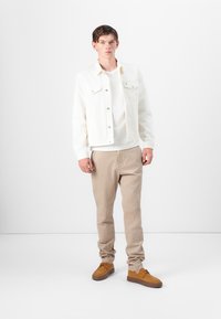 Hvid denimjakke over en hvid skjorte, parret med beige bukser og brune snørebåndsko; har et simpelt design og lyse neutrale farver.