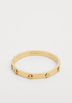 Gold metal bangle bracelet featuring a smooth finish with three decorative accents and a hinge closure; brand engraved on the interior.
