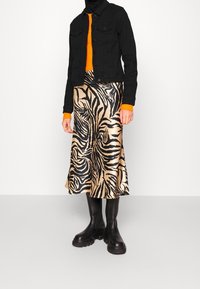 Veste en denim noire, pull à côtes orange, jupe en satin doré avec des rayures zèbre noires, et bottes noires à semelle épaisse. Texture lisse tout au long.