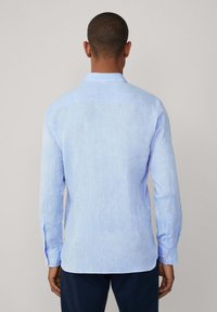 Camicia azzurro chiaro a maniche lunghe in tessuto texturizzato. Presenta un colletto classico e polsini con bottone, con un orlo leggermente curvo.