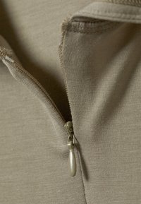 Khaki zippered garment with a ribbed texture; features a light-colored zipper with a tab for easy handling. Close-up view highlights details.