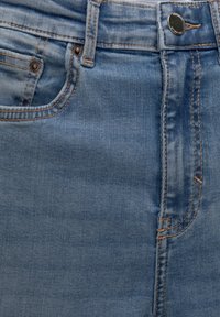 Jean en denim bleu présentant une taille mi-haute, un design classique à cinq poches et des surpiqûres orange contrastantes le long des coutures.