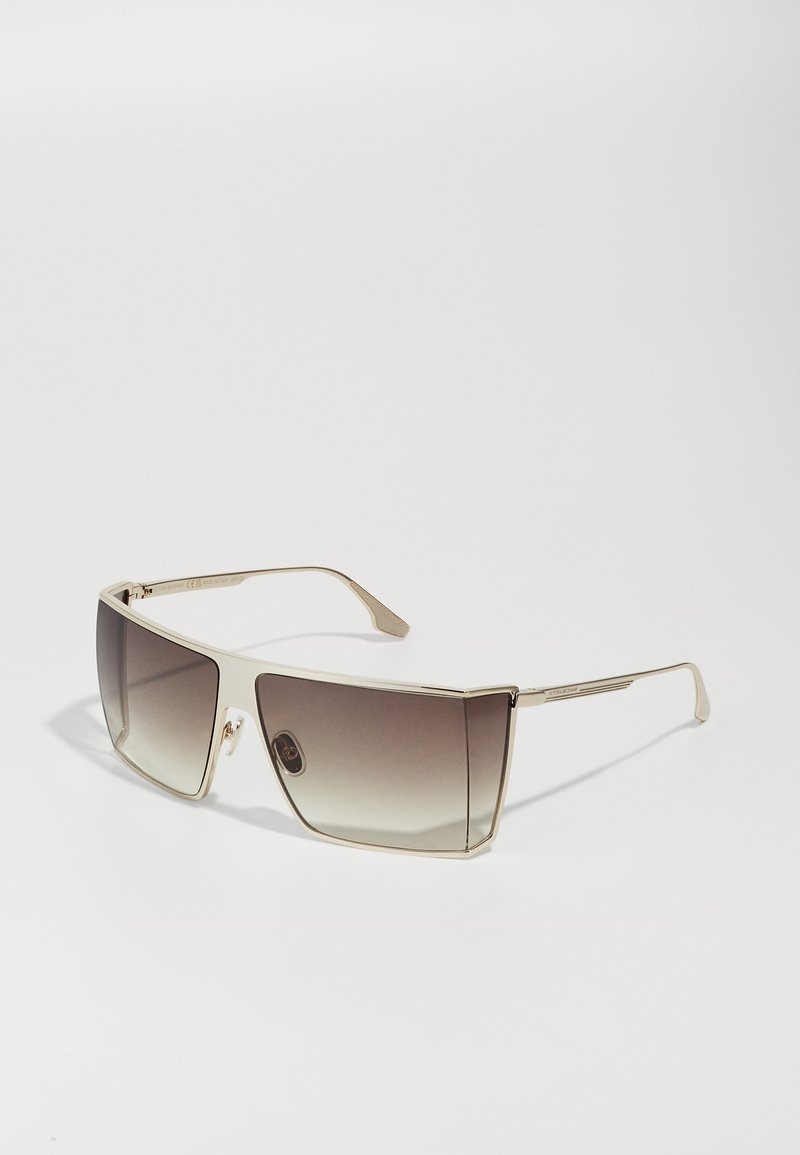 Lunettes de soleil au grand format carré. Monture en métal doré avec des verres bruns dégradés. Présente des accents matériels fins près des branches.